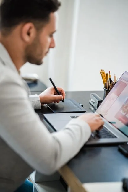 A silhouette of a fashion designer examining a creative mood board filled with fashion sketches and photos.